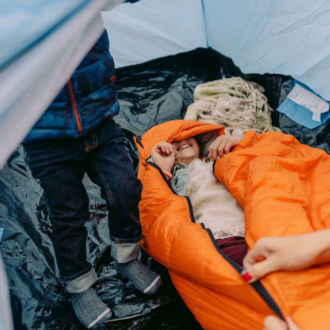 Young girl smiling in orange sleeping bag inside family camping tent
