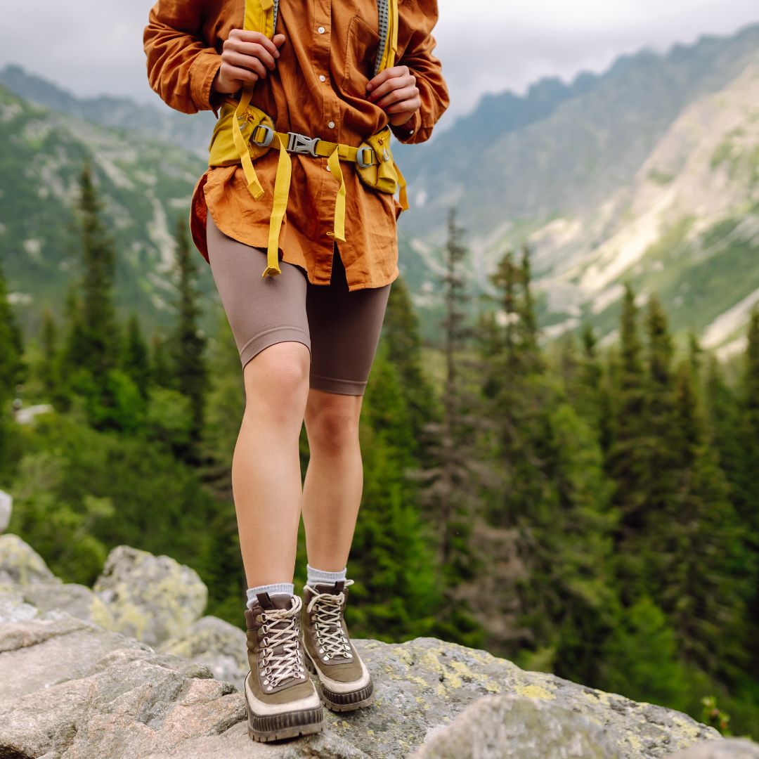Person hiking in a mountainous area with greenery and rocky terrain.