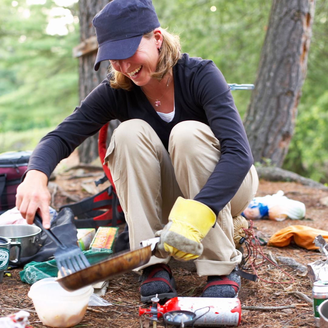 Happy woman cooking breakfast in pan at forest camping site