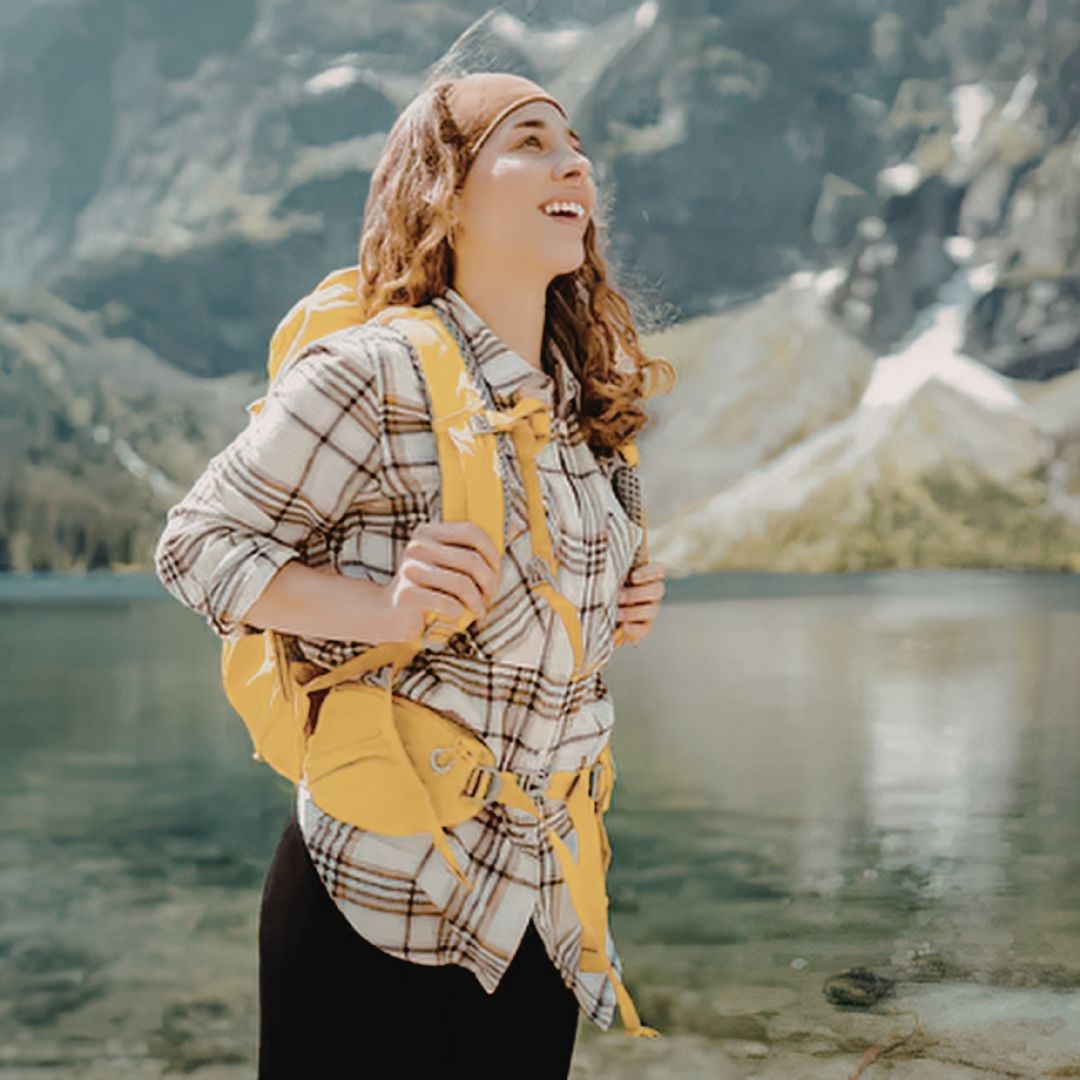 Smiling woman with yellow backpack hiking by scenic mountain lake
